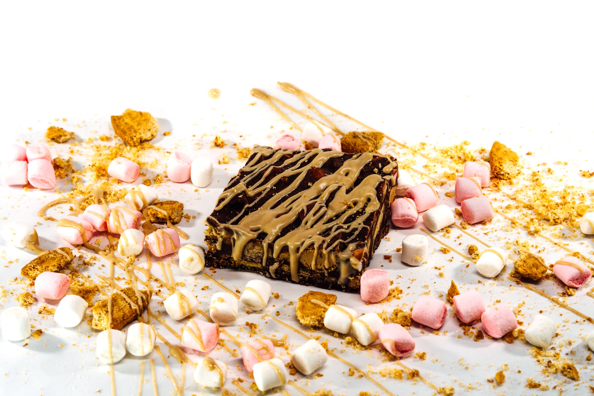A chocolate bake topped with caramel drizzle, surrounded by biscuit crumbs and marshmallows